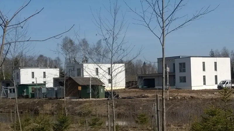 Keli statomi balti dviejų aukštų namai su plokščiais stogais, priekyje jauni medžiai