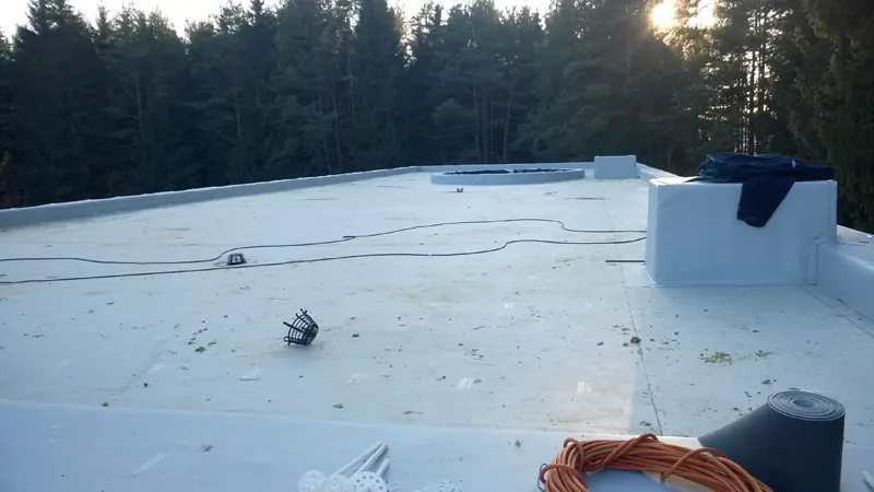 Šviesios membranos plokščias stogas su parapetais, fone miškas ir žema saulė